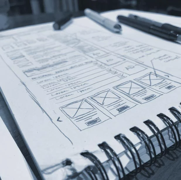 A closeup view of sketchbook showing drawn wireframes of the website design